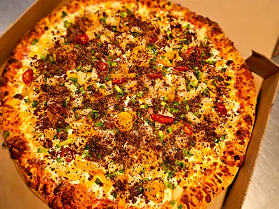 A cheeseburger pizza with pineapple and banana peppers